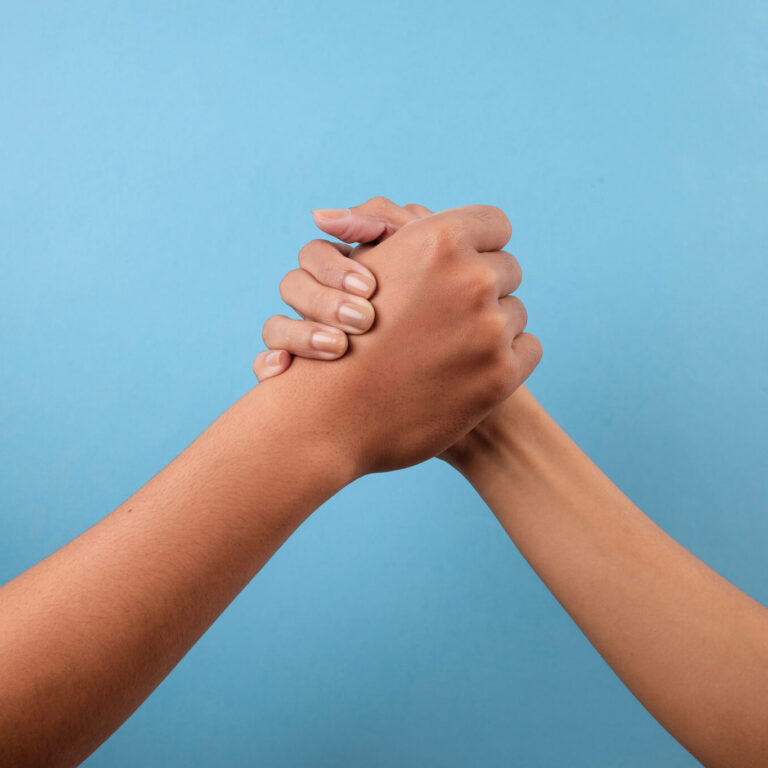 Two hands tightly interlaced in a clasp against a blue background.